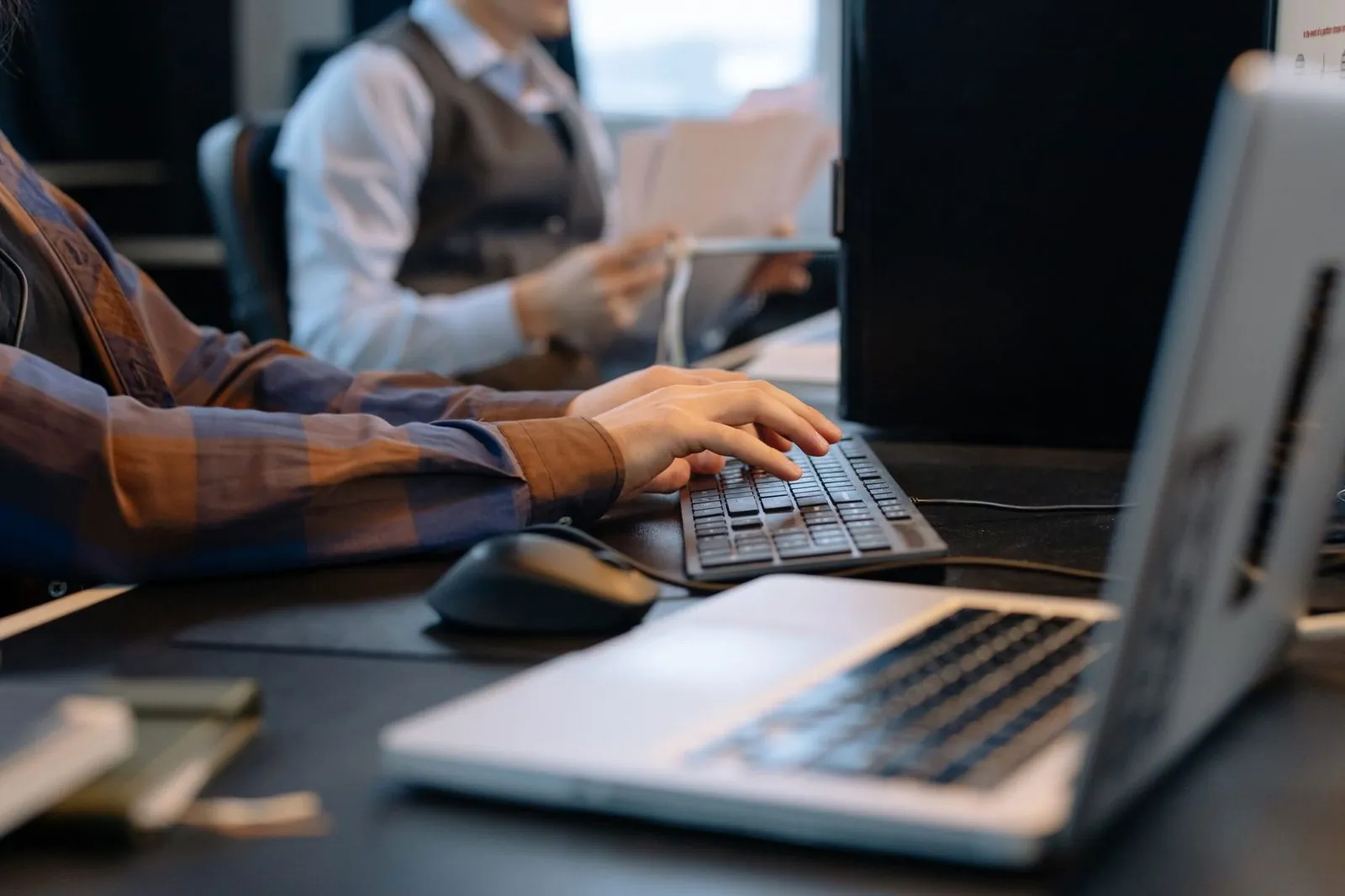 Manos escribiendo en el teclado en un puesto de trabajo de oficina